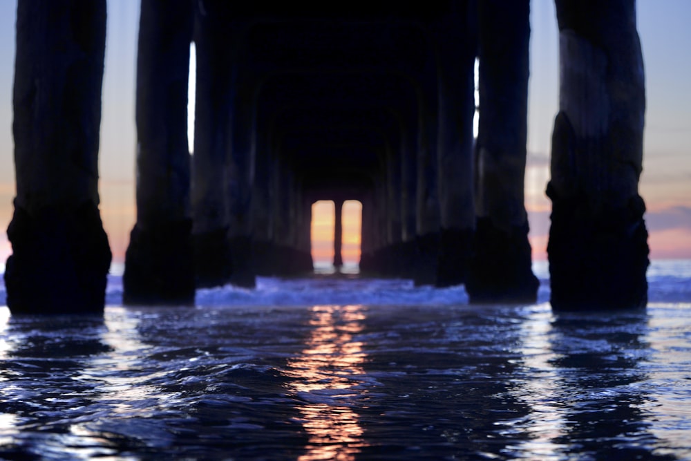 a view of the ocean under a pier at sunset