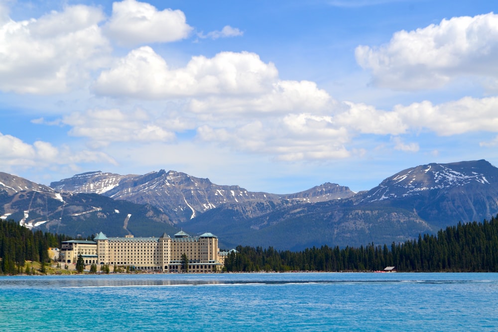 a large building sitting on top of a lake surrounded by mountains