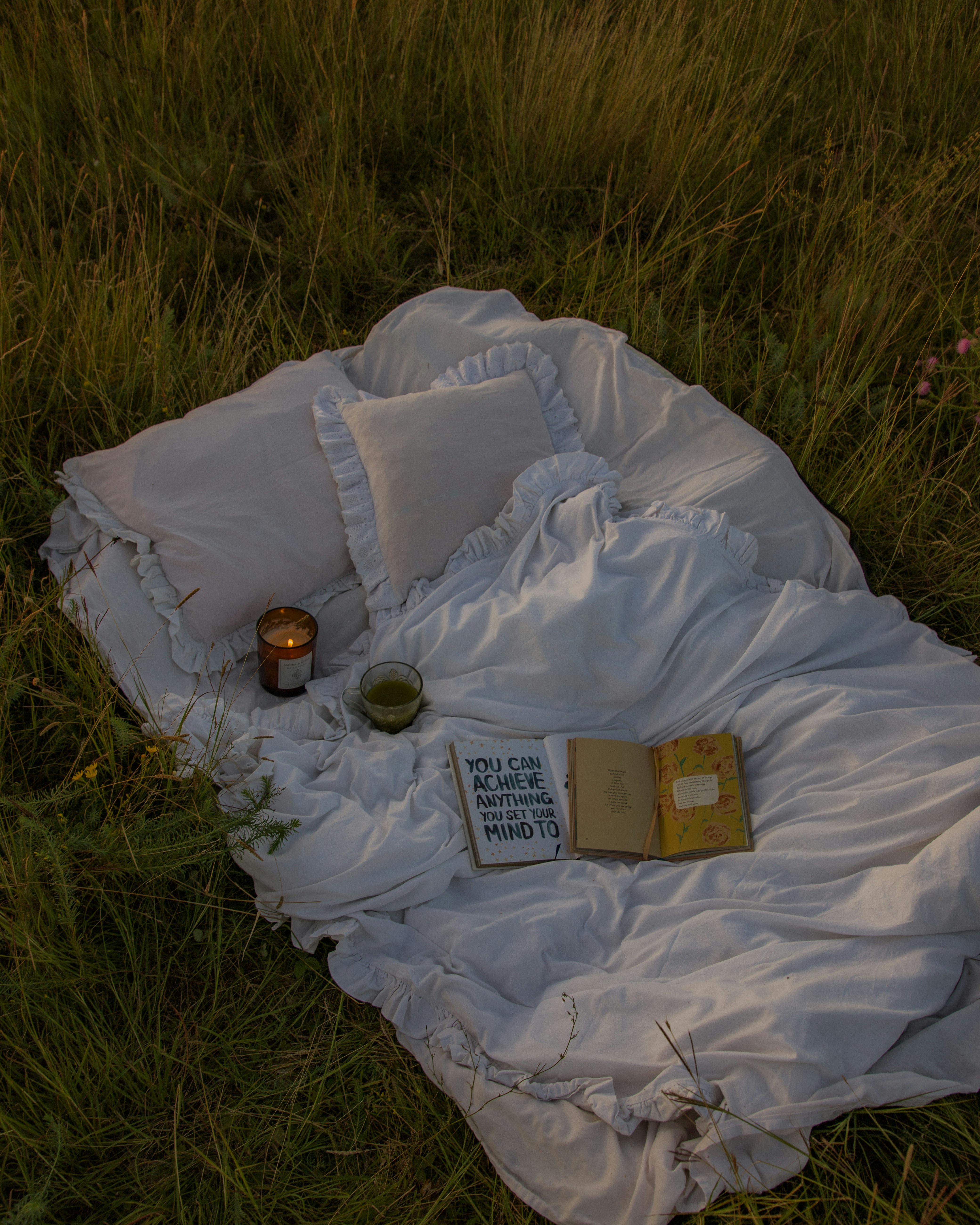 Outdoor healing space with pillows, candles, books, and a soft summer sunset glow