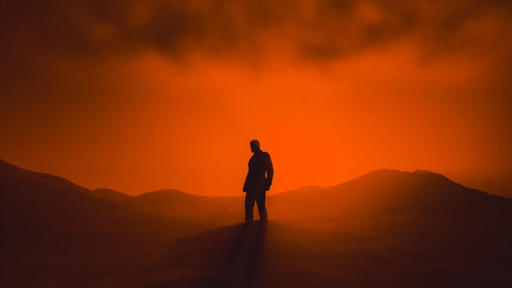 un hombre de pie en la cima de una colina bajo un cielo rojo