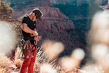 A candid shot of a climber adjusting their gear with a forested mountain slope behind.