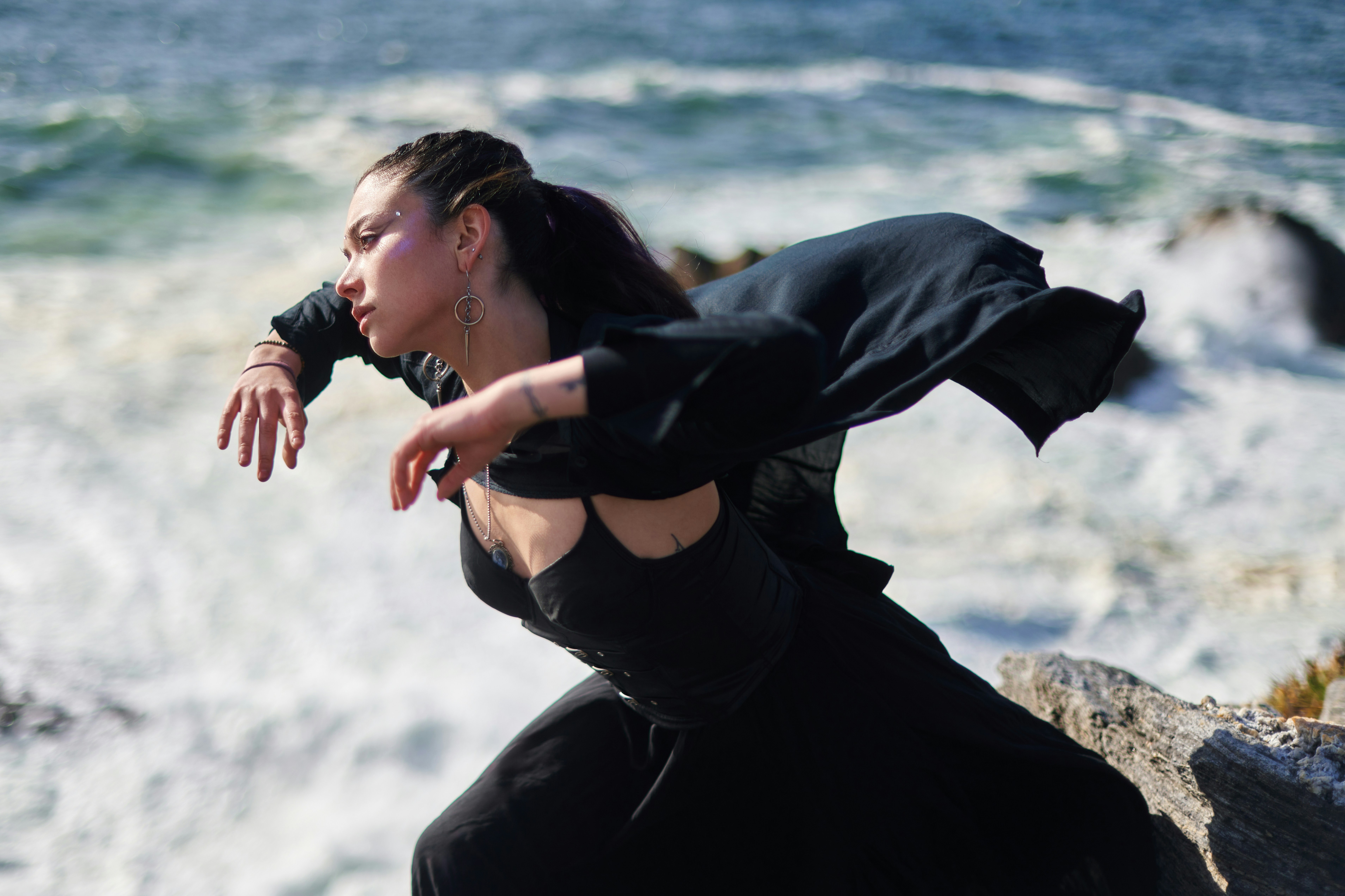 a woman standing on a rock near the ocean, 