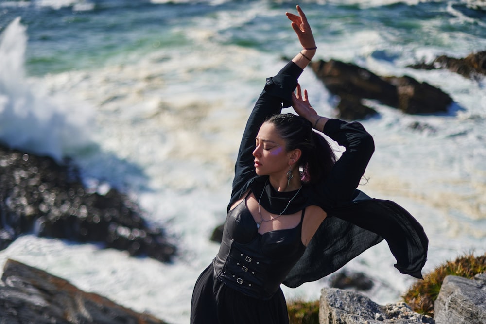 a woman in a black dress standing on a rock by the ocean