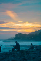 A serene beach scene with a luxury resort silhouetted against a vibrant sunset sky.