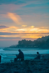 A serene beach with travelers relaxing under palm trees at sunset.