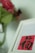 A close-up of a white-framed image featuring Chinese calligraphy on a red background. In the blurred background, there is a vase with pink and red flowers.