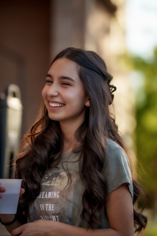 Young woman holding a bright pink hand-painted phone case smiling outdoors