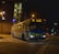A city bus is traveling at night, illuminated by streetlights. The bus is clearly marked with the route number 352 and destination Ocean Park. The scene includes an urban setting with buildings, trees, and traffic lights visible in the background. A few cars can be seen on the road behind the bus.