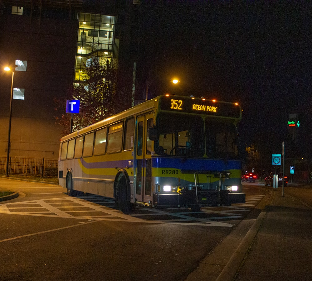 a yellow and blue bus driving down a street at night