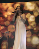 A soprano in a flowing red gown passionately singing under warm stage lights.