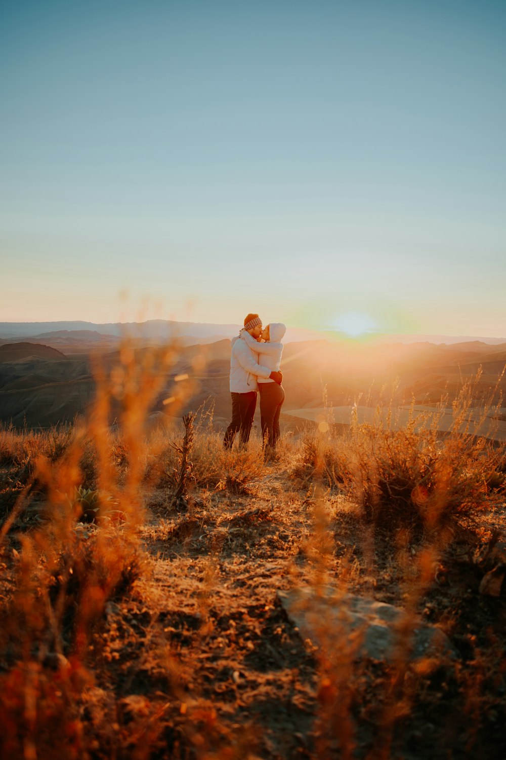 a man and woman standing on top of a grass covered hillside