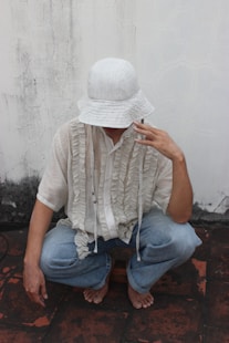 a man sitting on the ground wearing a white hat