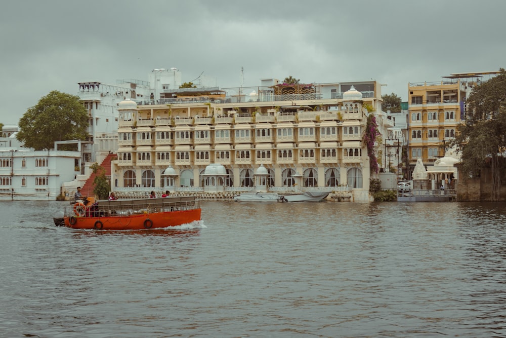 a red boat in a body of water near a large building