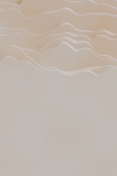 Soft, undulating curves resembling gentle hills or waves create a calming, minimalist scene. The smooth, light beige tones add to the serene atmosphere.