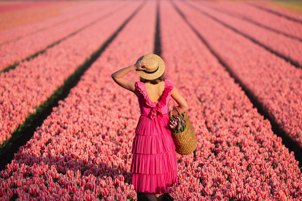 a woman in a pink dress and hat standing in a field of flowers