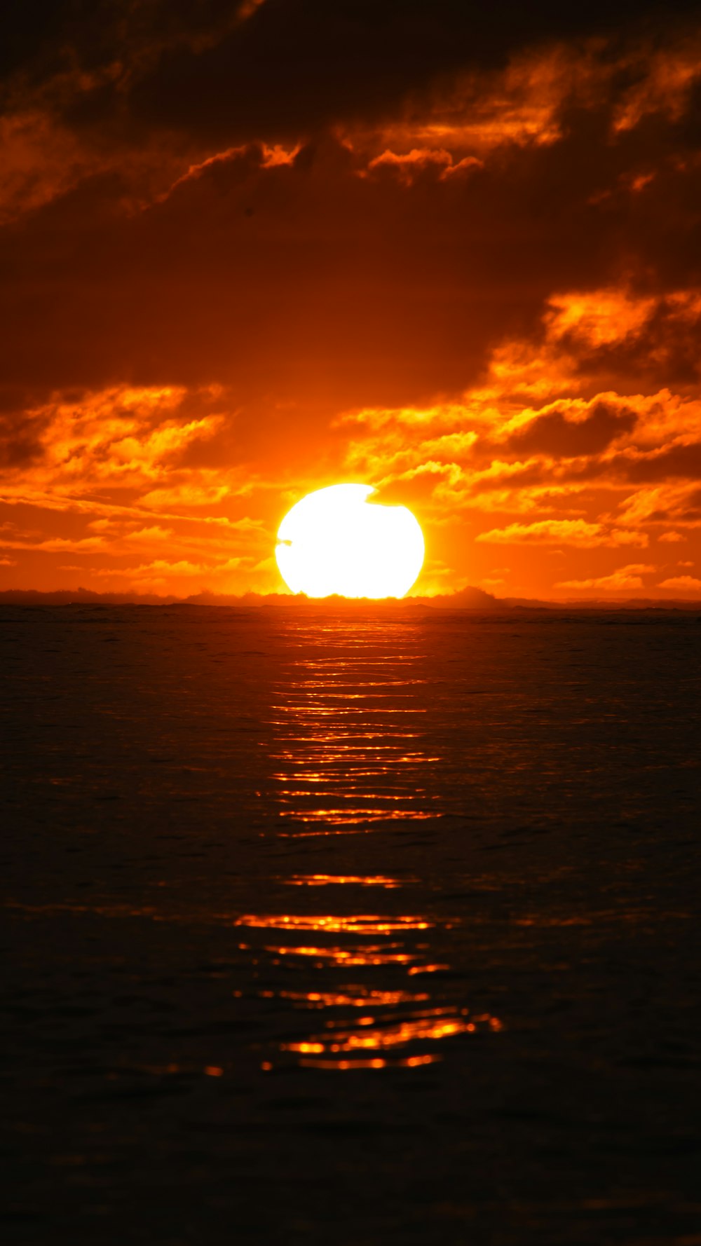 the sun is setting over the ocean on a cloudy day