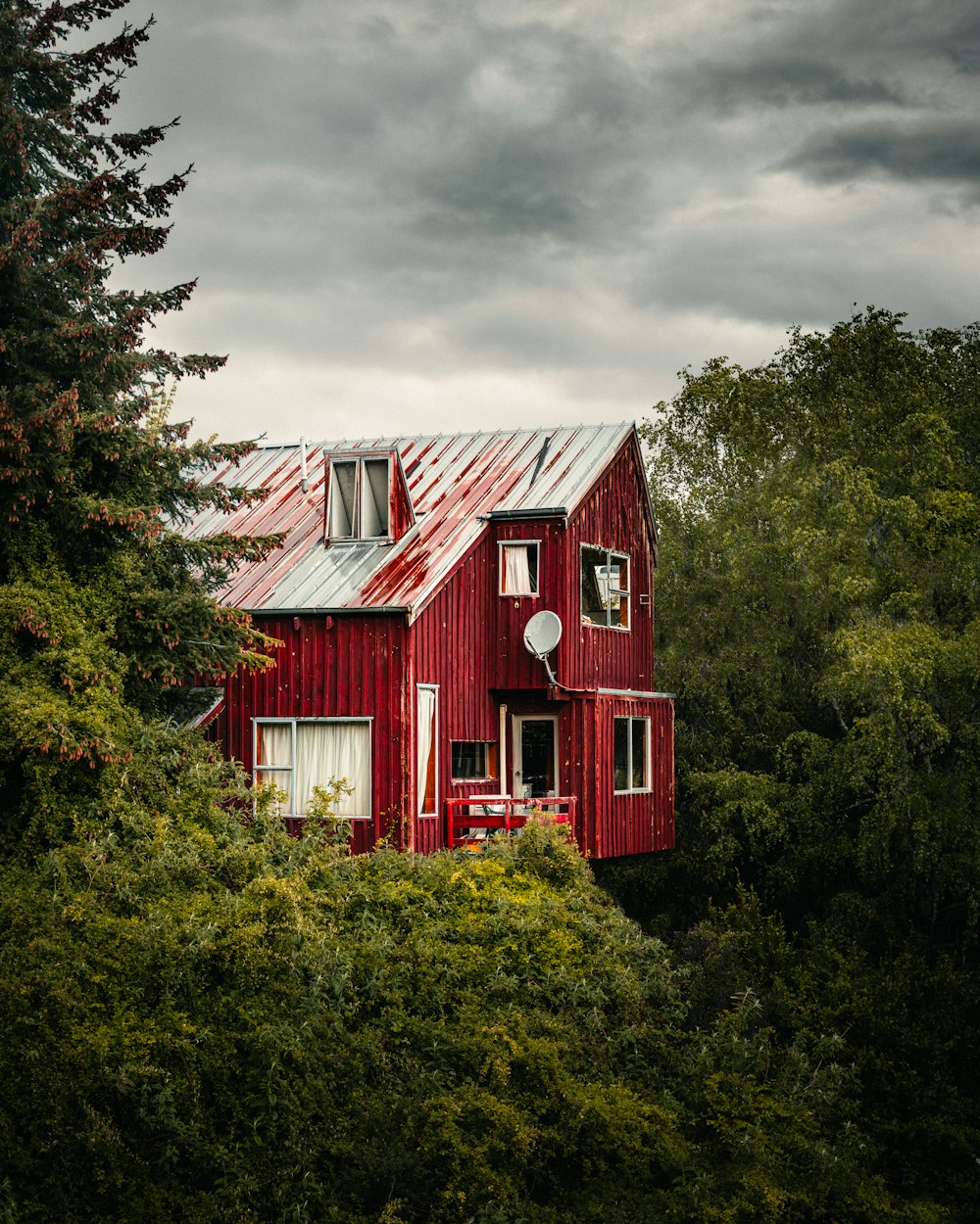 a red house surrounded by trees under a cloudy sky