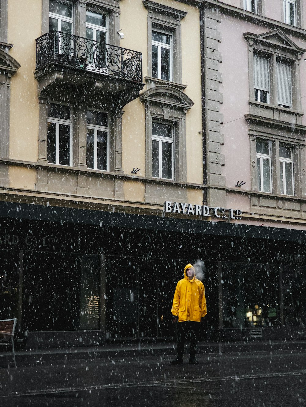 eine Person in einem gelben Regenmantel steht vor einem Gebäude