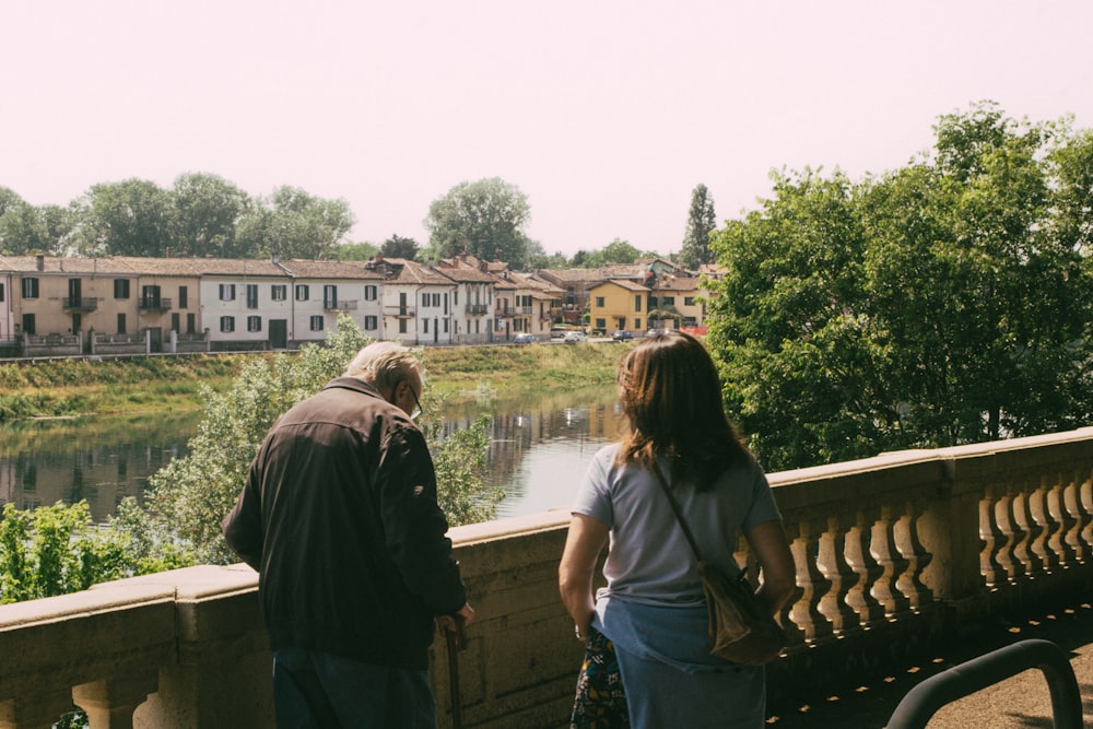 a man and a woman standing on a bridge looking at a river