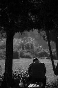 A serene image of a person sitting alone on a park bench, gazing thoughtfully into the distance, surrounded by nature.