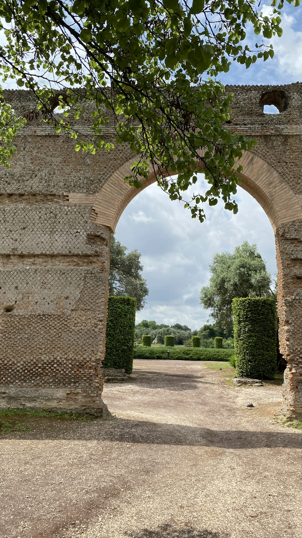 an arch in a stone wall with a dirt road leading to it