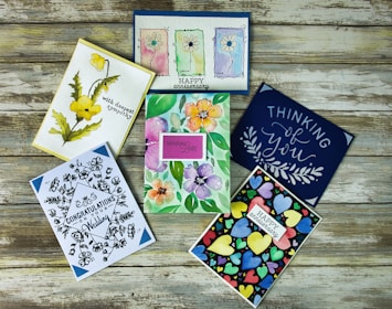 Flat lay of illustrated greeting cards, stickers, and prints on a lavender-toned surface.