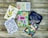 Six colorful greeting cards are arranged on a rustic wooden surface. The cards feature a variety of designs including floral illustrations, abstract heart patterns, and cursive text. Themes include sympathy, congratulations, and love.