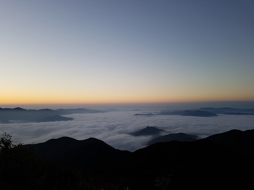 the sun is setting over the mountains above the clouds