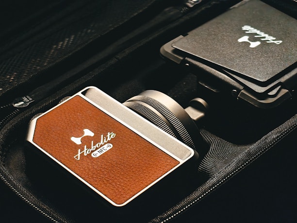 A close-up view of a device with a brown leather-like texture, branded 'Hobolite' and labeled with 'NFC' in a sleek, metallic case. The device is positioned next to a folded item with another 'Hobolite' label, all placed within a black fabric bag or case.