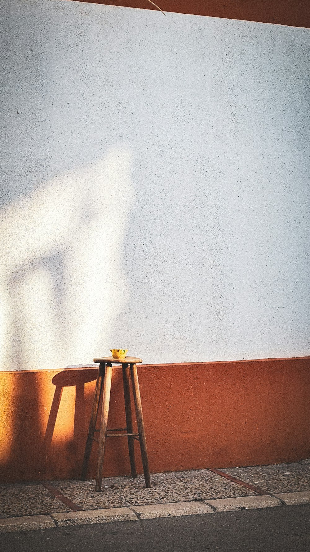 a wooden stool sitting next to a white wall