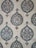 The image showcases a detailed pattern of decorative ceramic tiles. Each tile features intricate floral and geometric designs primarily in shades of blue, green, and white, with accents of brown. The repeating pattern consists of a central floral motif encased within a teardrop shape adorned with foliage and symmetrical designs extending outward.