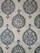 The image showcases a detailed pattern of decorative ceramic tiles. Each tile features intricate floral and geometric designs primarily in shades of blue, green, and white, with accents of brown. The repeating pattern consists of a central floral motif encased within a teardrop shape adorned with foliage and symmetrical designs extending outward.