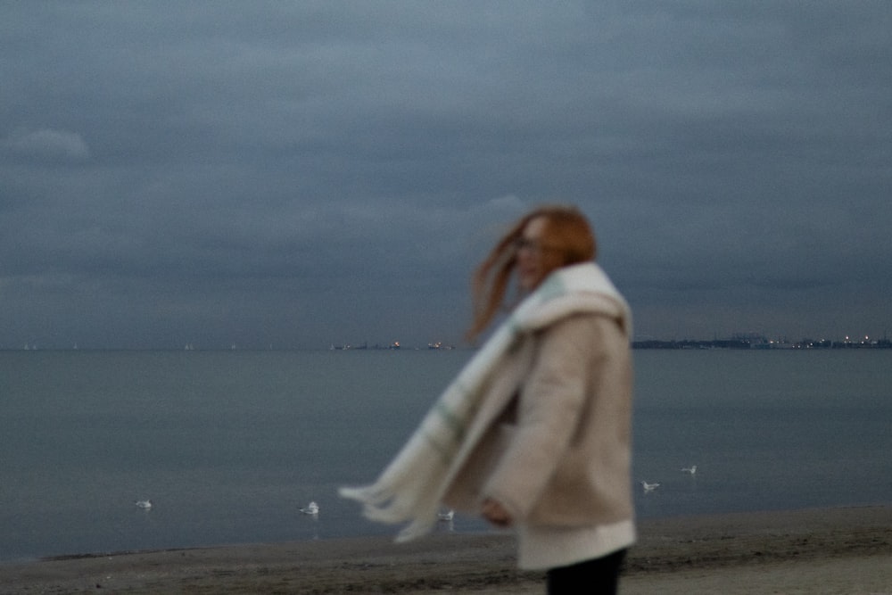 a woman walking on a beach with a scarf around her neck