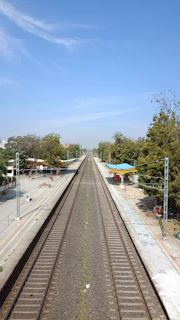 Wide shot of a quiet rural station with a single train waiting on the tracks under a blue sky