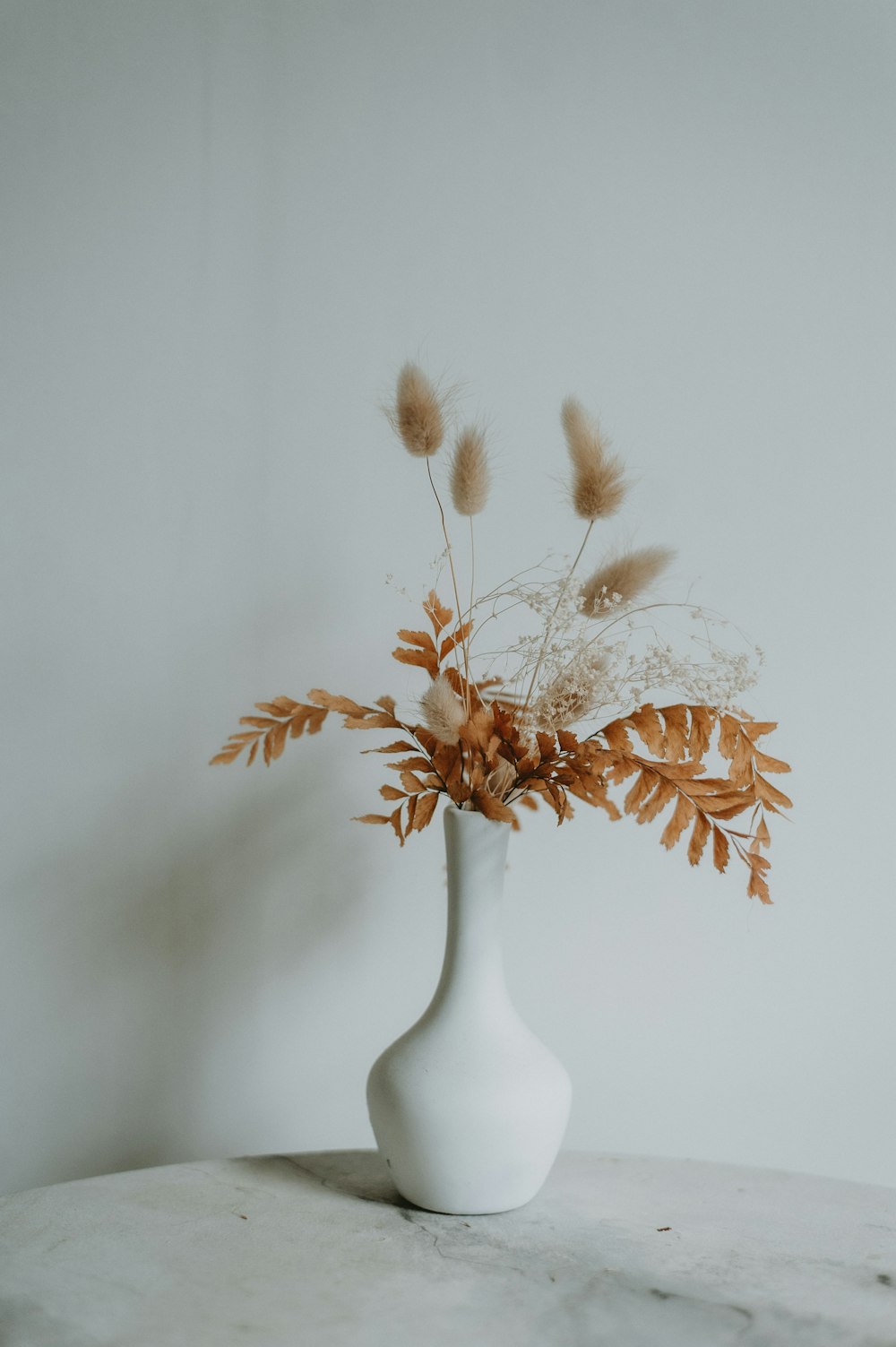 un jarrón blanco lleno de flores encima de una mesa