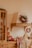 A cozy kitchen setting featuring a wooden cabinet and countertop. Decorative wreaths with red berries and green foliage adorn the walls. There is a collection of wooden cutting boards and kitchen utensils, with red mugs and a fresh loaf of bread placed on a patterned cloth. A warm, inviting ambiance is emphasized by rustic elements and natural materials.