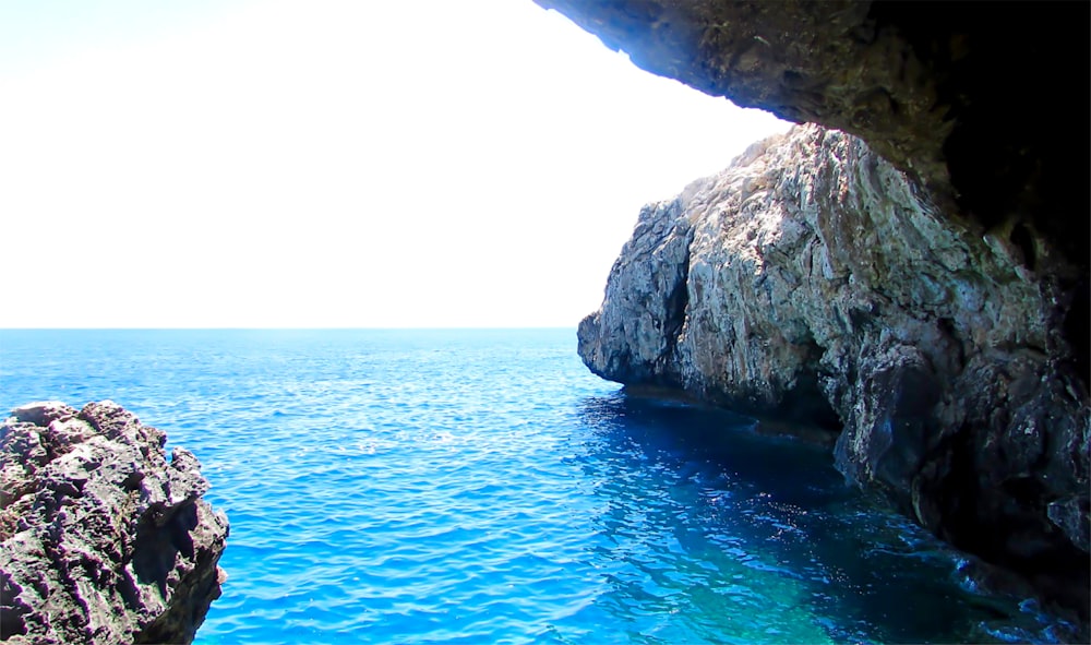 a large rock sticking out of the ocean next to a cliff