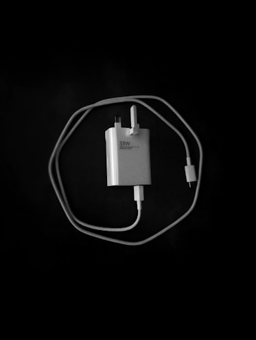 A power adapter with a plug and cable, labeled '33W,' centrally positioned against a dark background. The cable is neatly coiled around the adapter, forming an almost circular shape.