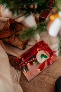 A cozy holiday scene featuring neatly wrapped gifts under a Christmas tree. One gift is wrapped in festive paper with a red ribbon, displaying a candle decorated with holly. The other gift is wrapped in brown paper with a dark brown ribbon, creating a warm and inviting atmosphere.