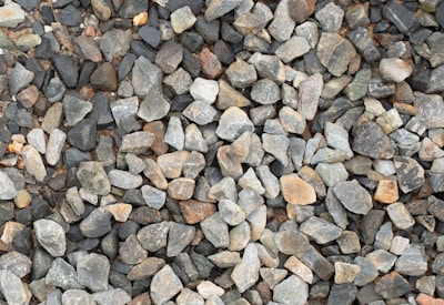 A large collection of irregularly shaped rocks and stones in various shades of gray, brown, and beige is closely packed together. The stones vary in size and texture, creating a natural and rugged surface.