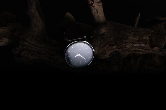 A sleek, minimalistic watch face resting on a clean white surface with soft shadows.