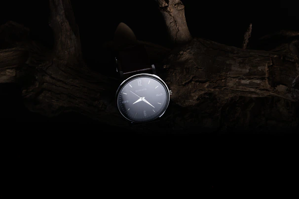 A modern watch face with clean lines and a subtle logo, photographed against a dark background.