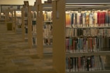 A library aisle with neatly aligned books on wooden shelves. The shelves are filled with a variety of books, with a focus on fiction and non-fiction genres. The environment is well-lit, providing a quiet and organized atmosphere typical of a library setting.