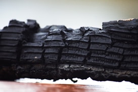 A close-up of charred wood showcasing layers of dark, burnt textures with visible cracks and lines. The background is blurred, highlighting the intricate details of the charred surface.