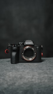 A dark-toned digital camera body with prominent branding and controls, placed on a soft, textured surface.
