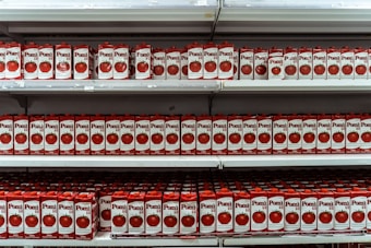 Numerous cartons of Pomi brand tomato sauce are arranged neatly on several shelves, creating a repetitive and organized pattern. The packaging features images of fresh tomatoes and bold red and white colors.