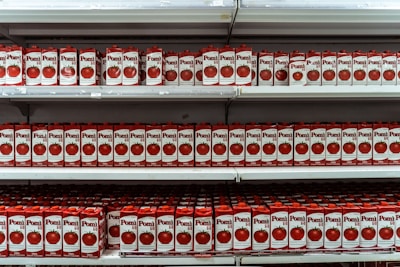 Numerous cartons of Pomi brand tomato sauce are arranged neatly on several shelves, creating a repetitive and organized pattern. The packaging features images of fresh tomatoes and bold red and white colors.