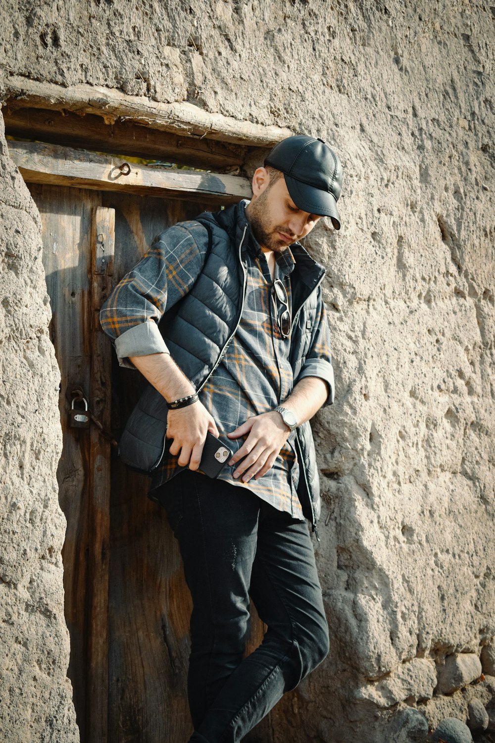 a man leaning against a door with a hat on