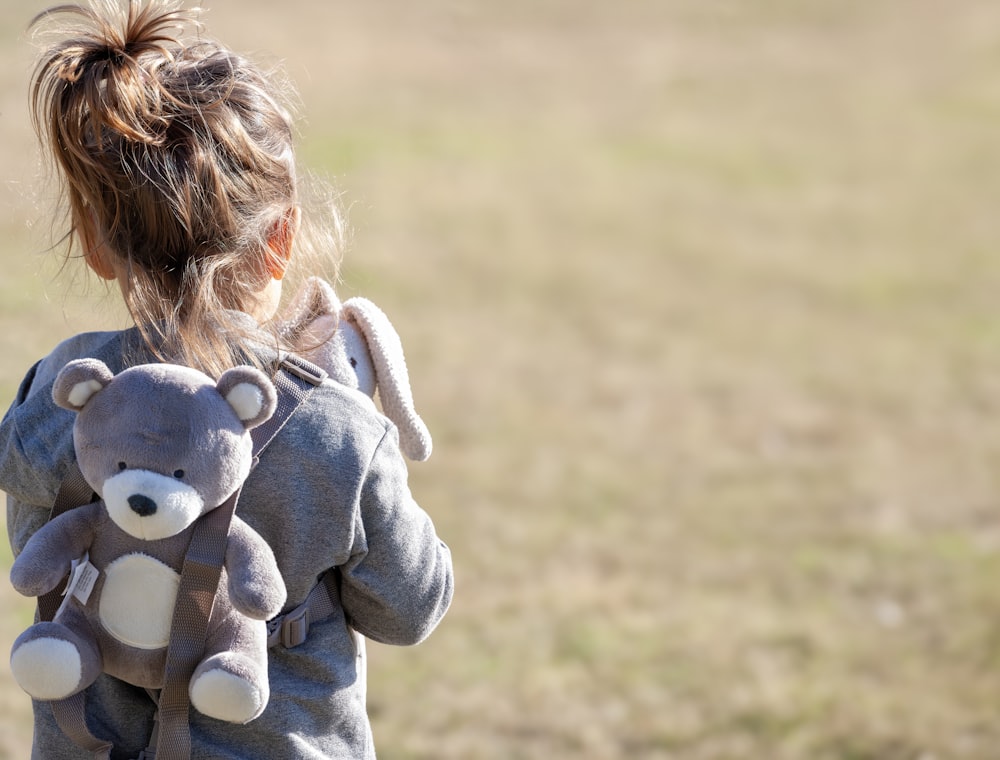 a little girl holding a teddy bear in a field