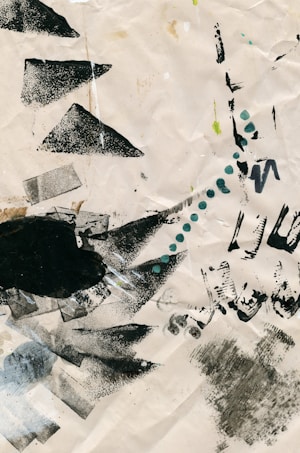 A textured paper background featuring various abstract shapes and marks including triangles, lines, and dots. Black paint smudges and green dots are distributed across the surface, creating a dynamic and unstructured design.